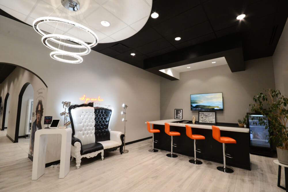 - Studio Wish Salon Spa in Twinsburg, OH Modern salon interior with a black and white throne-style chair, a counter with four orange stools, wall-mounted TV, and circular ceiling lights. Ideal for modern hair color or skincare facials amid light wood flooring and minimal decor. - Studio Wish Salon Spa in Twinsburg, OH