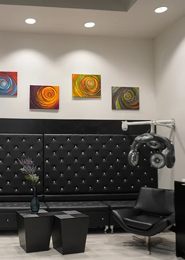 - Studio Wish Salon Spa in Twinsburg, OH Modern salon interior with a black tufted bench, a black salon chair, geometric tables, a vase with flowers, wall-mounted drying equipment, and colorful abstract paintings on the wall. - Studio Wish Salon Spa in Twinsburg, OH